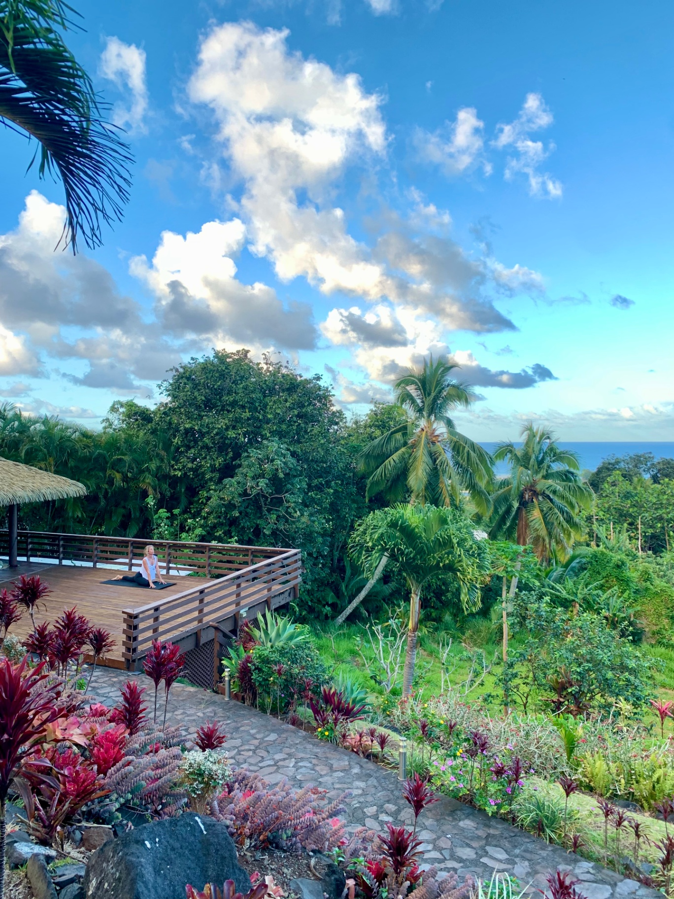 Woman practicing yoga on wooden deck overlooking tropical gardens and ocean